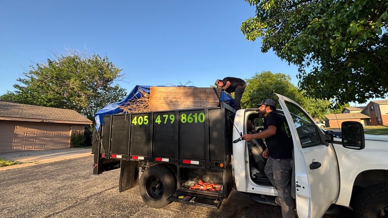 Worker loading hay into a dark green trailer attached to a white pickup truck on a sunny day