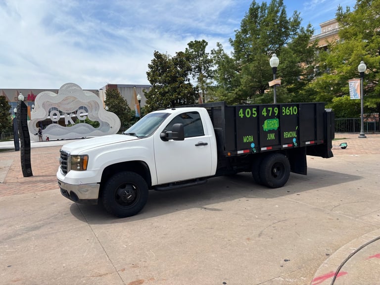 White and black junk removal truck parked in an urban plaza on a sunny day