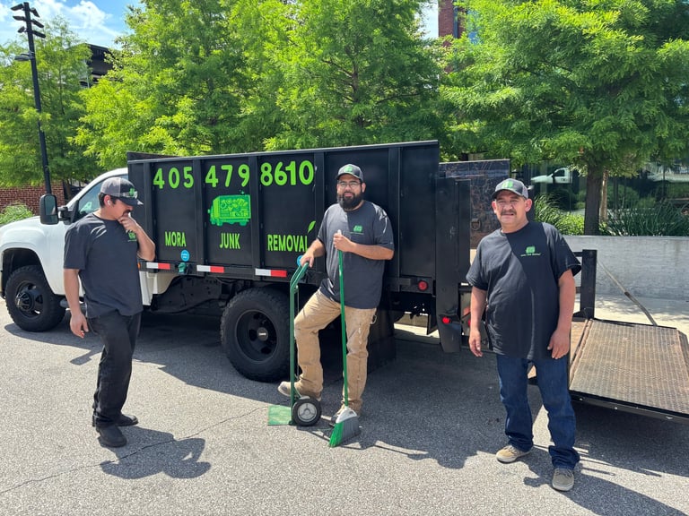 Four workers in dark uniforms stand with a black junk removal truck displaying phone number 405-479-8610 and green text