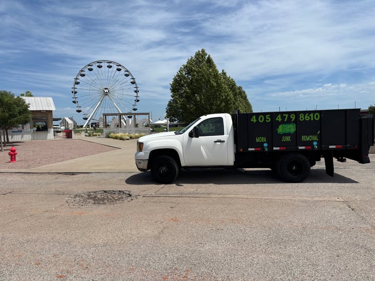 White commercial dumpster truck parked near a Ferris wheel at an amusement park or fairground