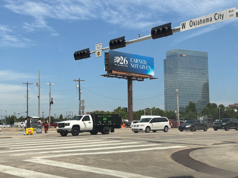 West Oklahoma City street intersection with traffic light, billboard sign, and vehicles under clear blue sky