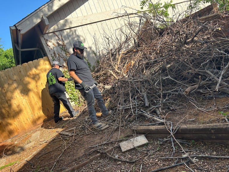 Two workers unloading wood debris from a dump truck into a pile of branches and yard waste