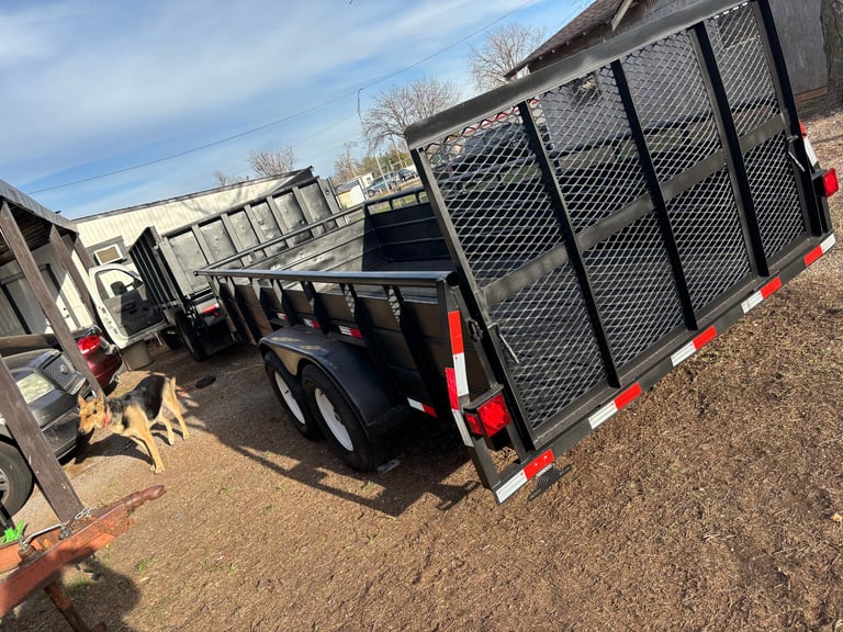 Row of black utility trailers with mesh sides and red reflectors parked on gravel lot
